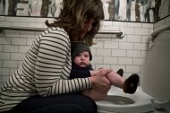 woman holding a diaperless baby over toilet